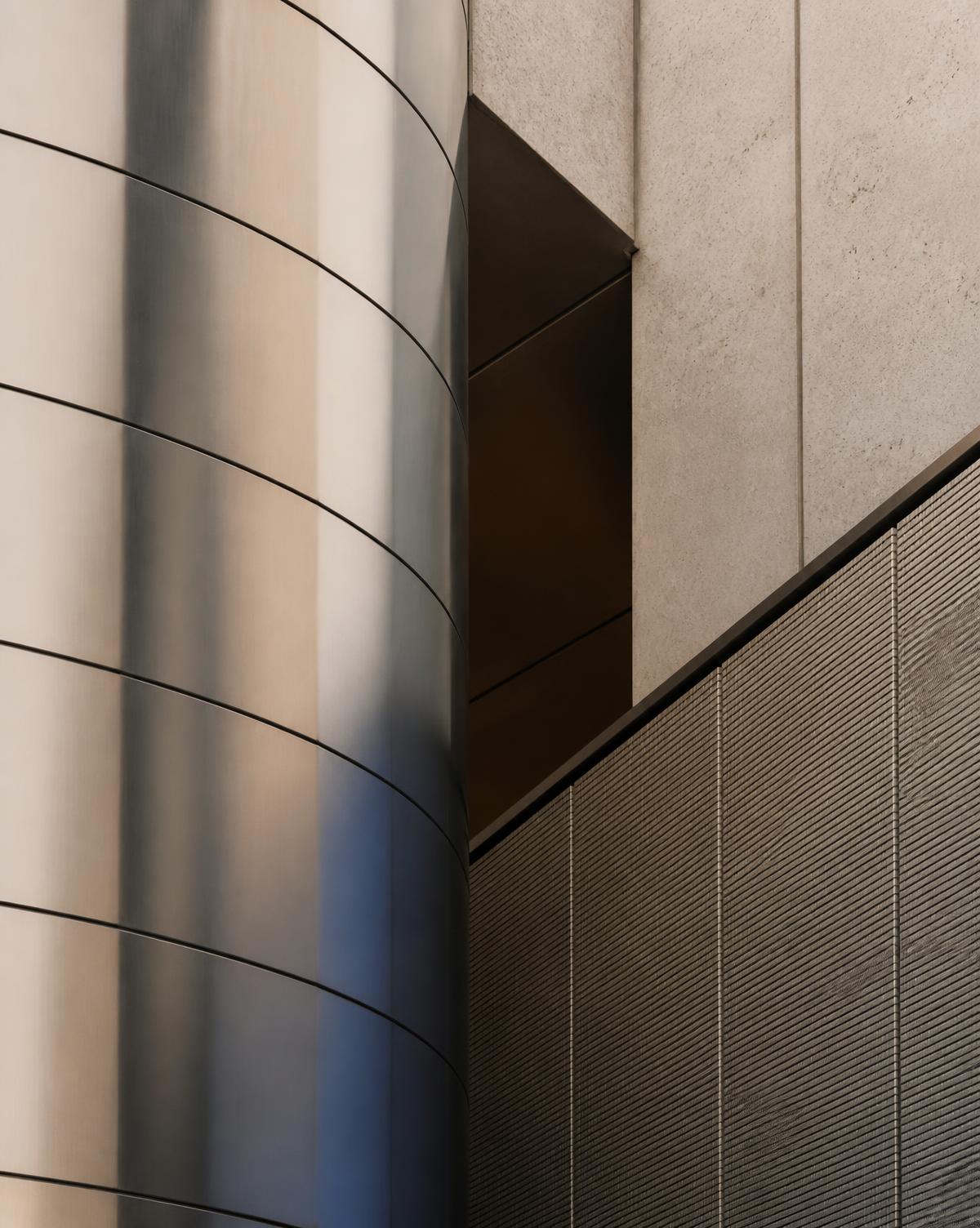Abstract architectural detail of a brushed metal facade meeting textured concrete
